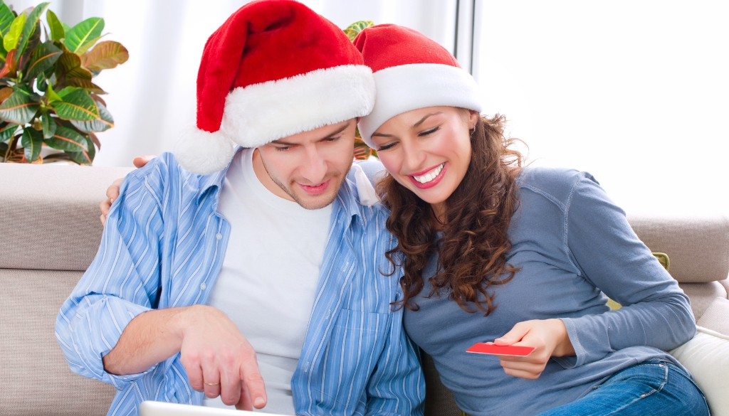 A couple wearing Santa hats makes an online shopping purchase.