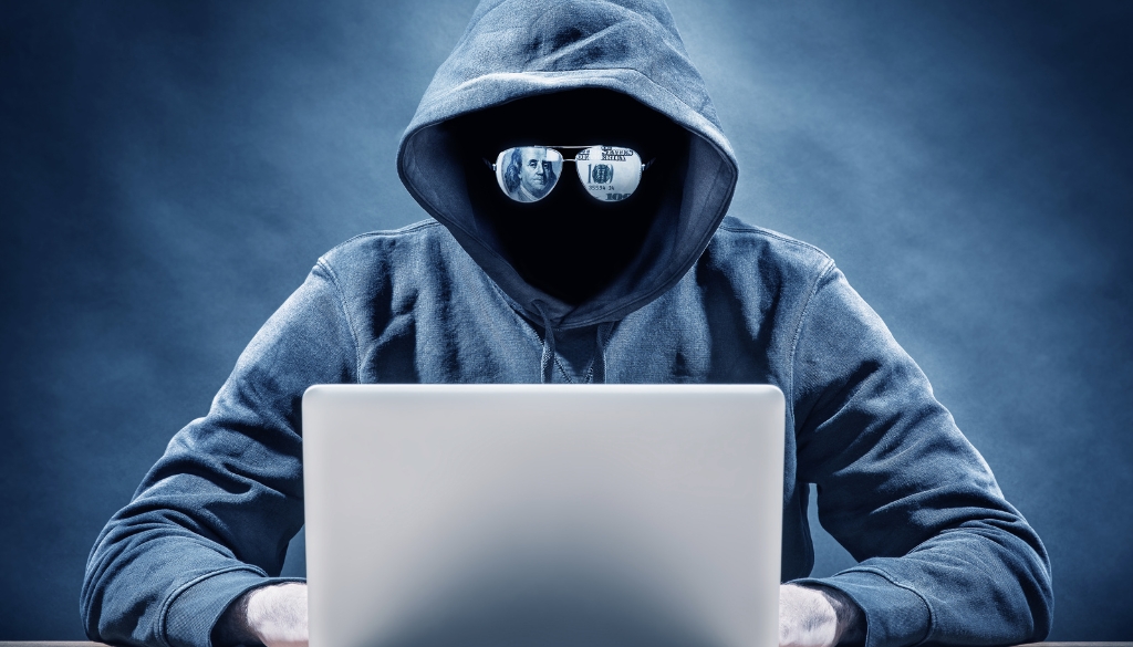 Masked person hacking into a laptop.