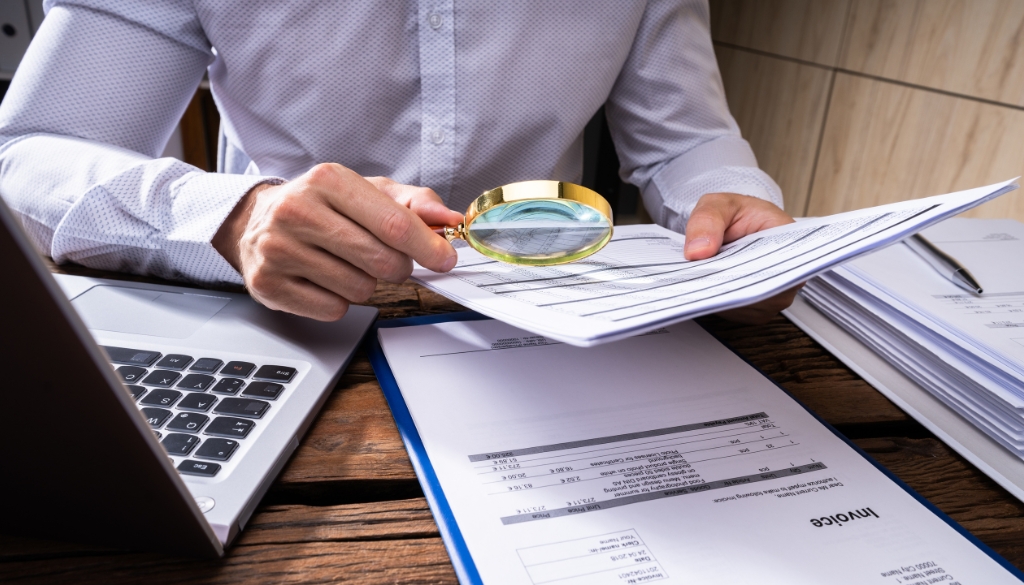 Detective using a magnifying glass to look at an invoice.