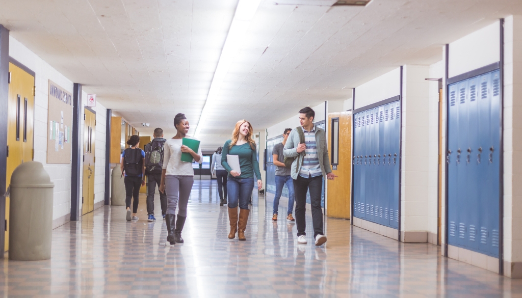 Back-to-School Security Tips: Protecting Students and School Property Three high school students holding school supplies talk while walking down the school hallway.
