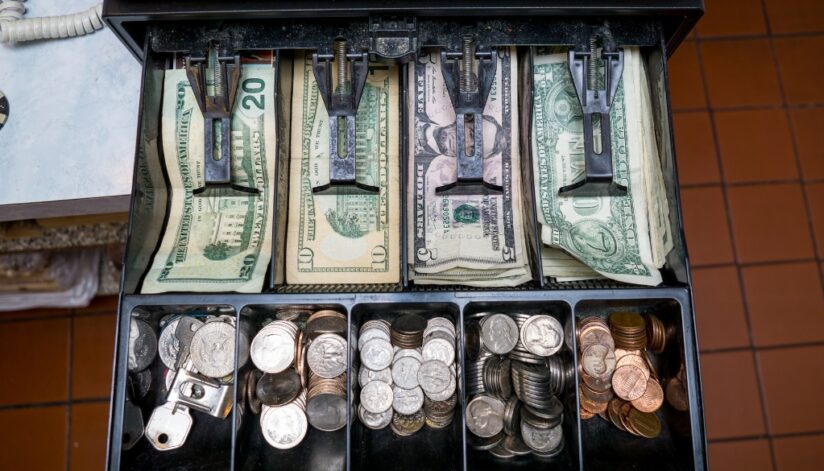 Cash register filled with various US dollar bills and change.