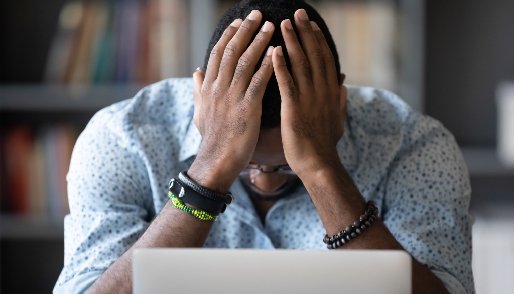 Man in despair holds his hands in front of his face while searching on his laptop.