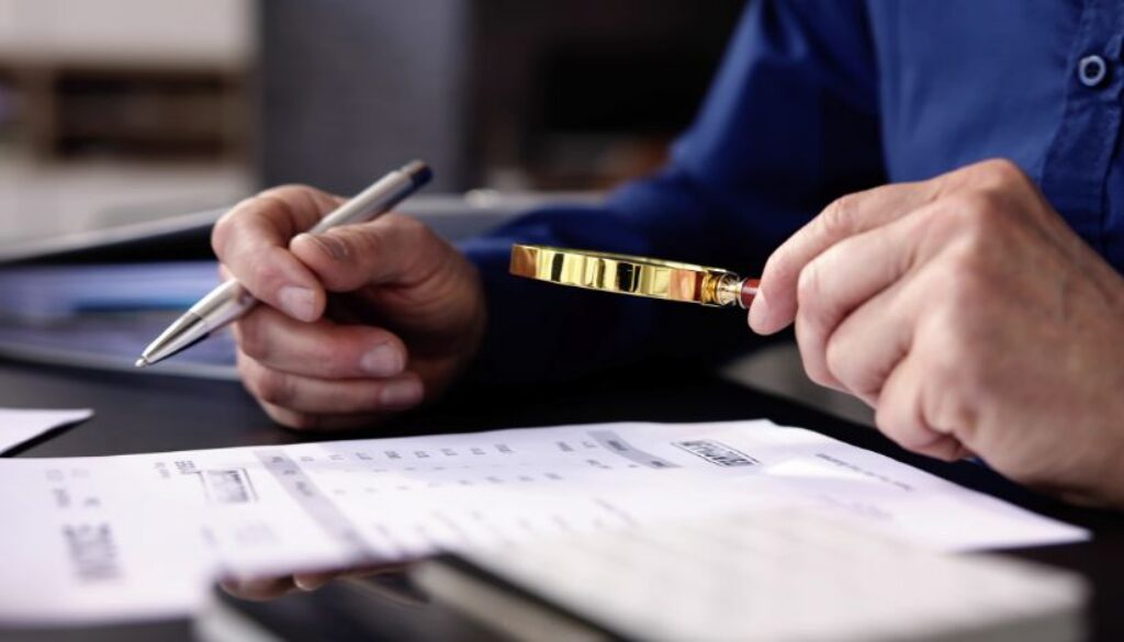 Private investigator looking through a magnifying glass at a stack of documents.