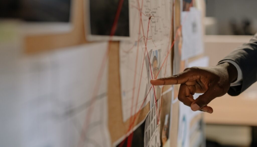 Private investigator pointing at a board of evidence trying to locate a missing person.