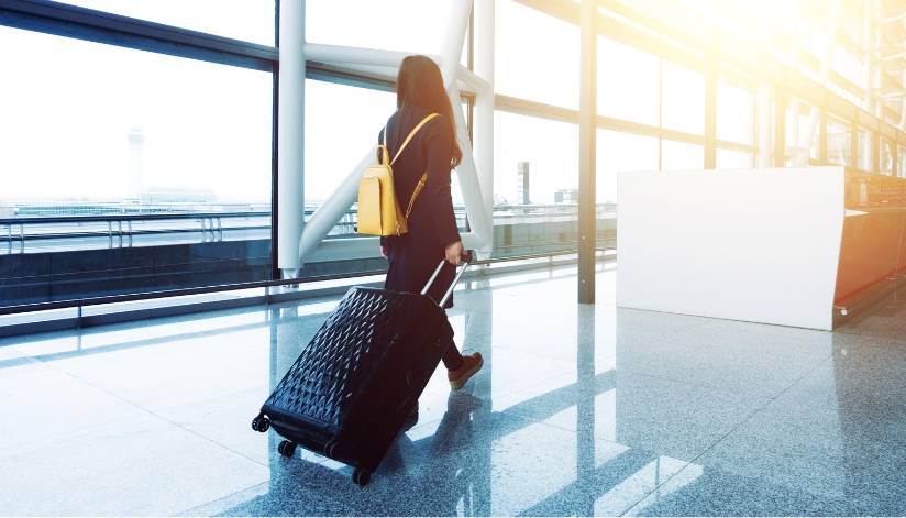 How To Protect Yourself And Your Family From Identity Theft While Traveling Woman walking through an airport with a suitcase.