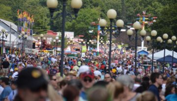 A large crowd of people gathering at a State Fair during summer.