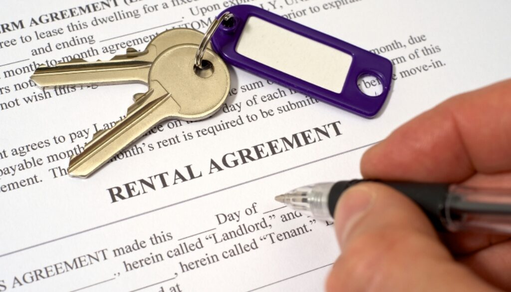 A person signing a rental agreement document with a set of keys on the paper.