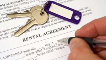 A person signing a rental agreement document with a set of keys on the paper.