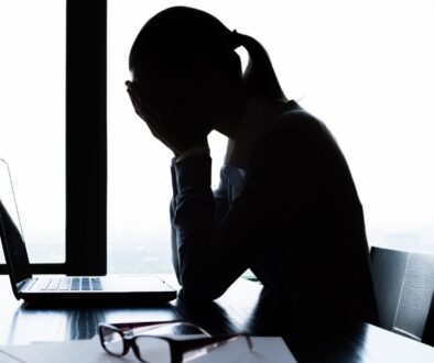 Woman sitting by a laptop with her hands over her face looking stressed.