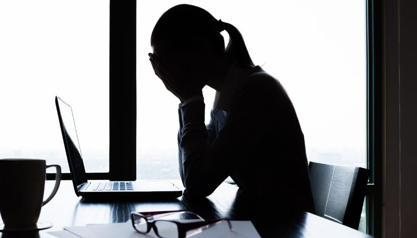 Woman sitting by a laptop with her hands over her face looking stressed.