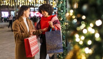 Two women holding festive holiday shopping bags and smiling.