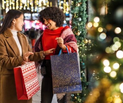 Two women holding festive holiday shopping bags and smiling.