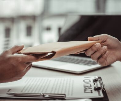 A private investigator handing a case file to a client, a contract is on the table below them.