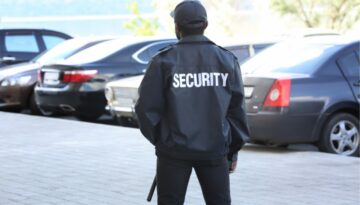A security guard standing in a parking lot monitoring traffic.