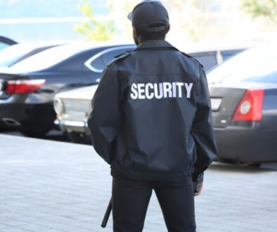 A security guard standing in a parking lot monitoring traffic.