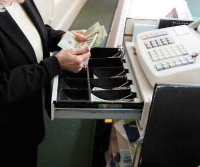 An employee counting twenty dollar bills in a cash register.