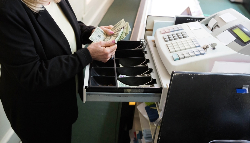 An employee counting twenty dollar bills in a cash register.
