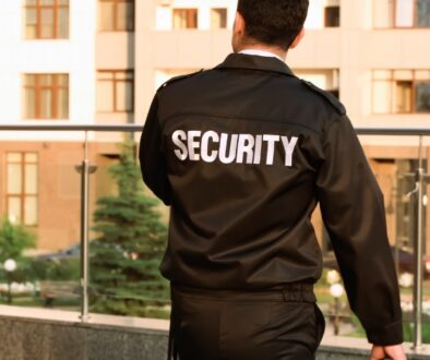 Security Guard faces away from lens, looking over a glass balcony towards green plants.