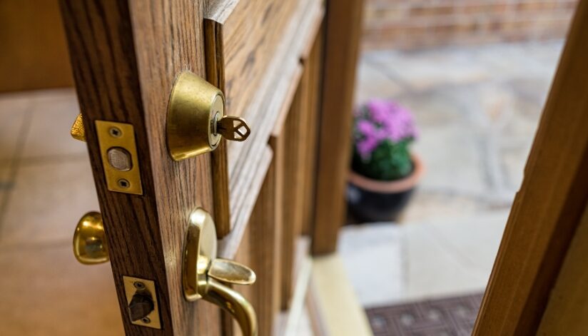 Wooden door that is ajar with a key in the deadbolt