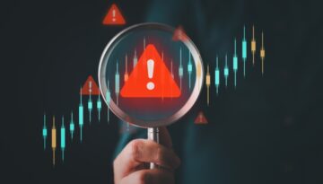 Hand holding up magnifying glass with a red triangle in the center with a white excalimation point.