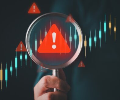 Hand holding up magnifying glass with a red triangle in the center with a white excalimation point.