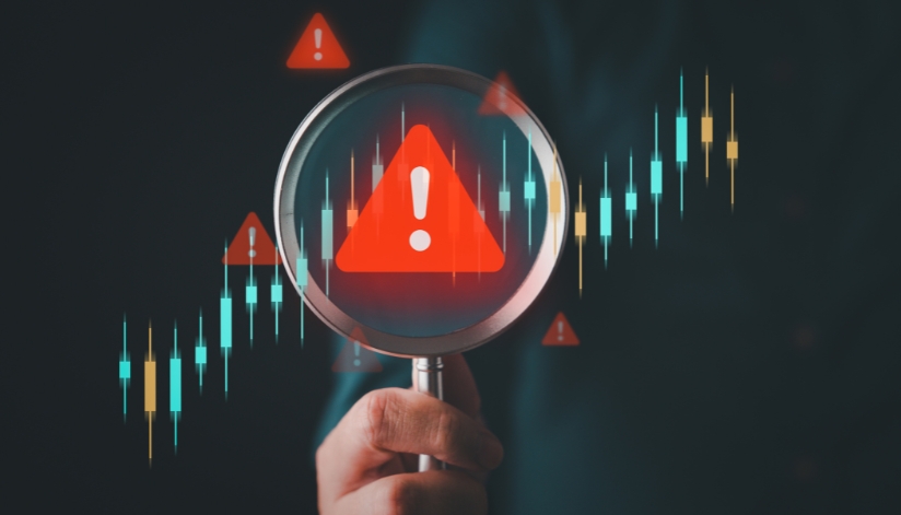 Hand holding up magnifying glass with a red triangle in the center with a white excalimation point.