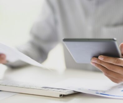Person holding a piece of paper in one hand and a tablet in the other.
