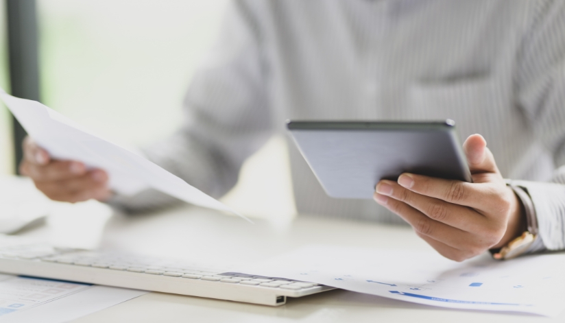 Person holding a piece of paper in one hand and a tablet in the other.